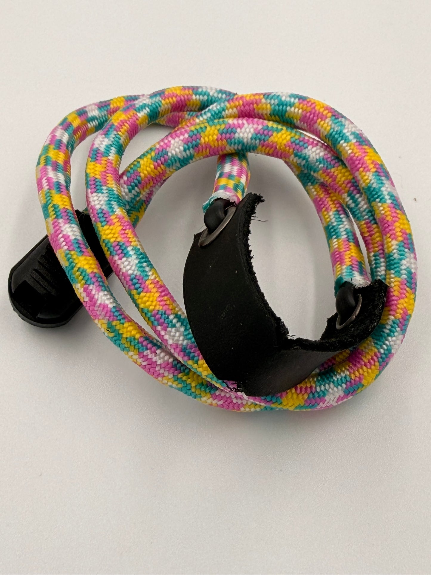 A coiled multicolored EDC bracelet with a black plastic buckle and a black leather basket, photographed on a plain light background.