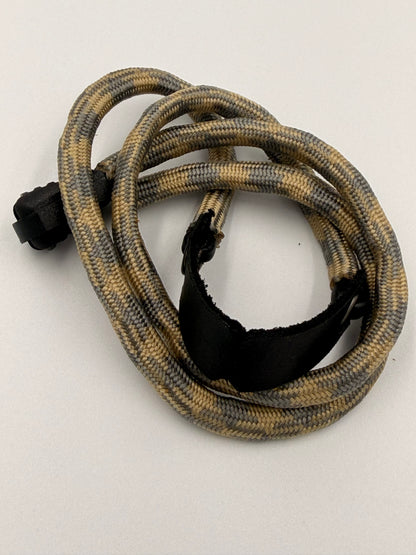 A coiled EDC bracelet with a tan and grey camouflage pattern, featuring a black plastic connector at one end and a black basket at the other, photographed on a plain light background.