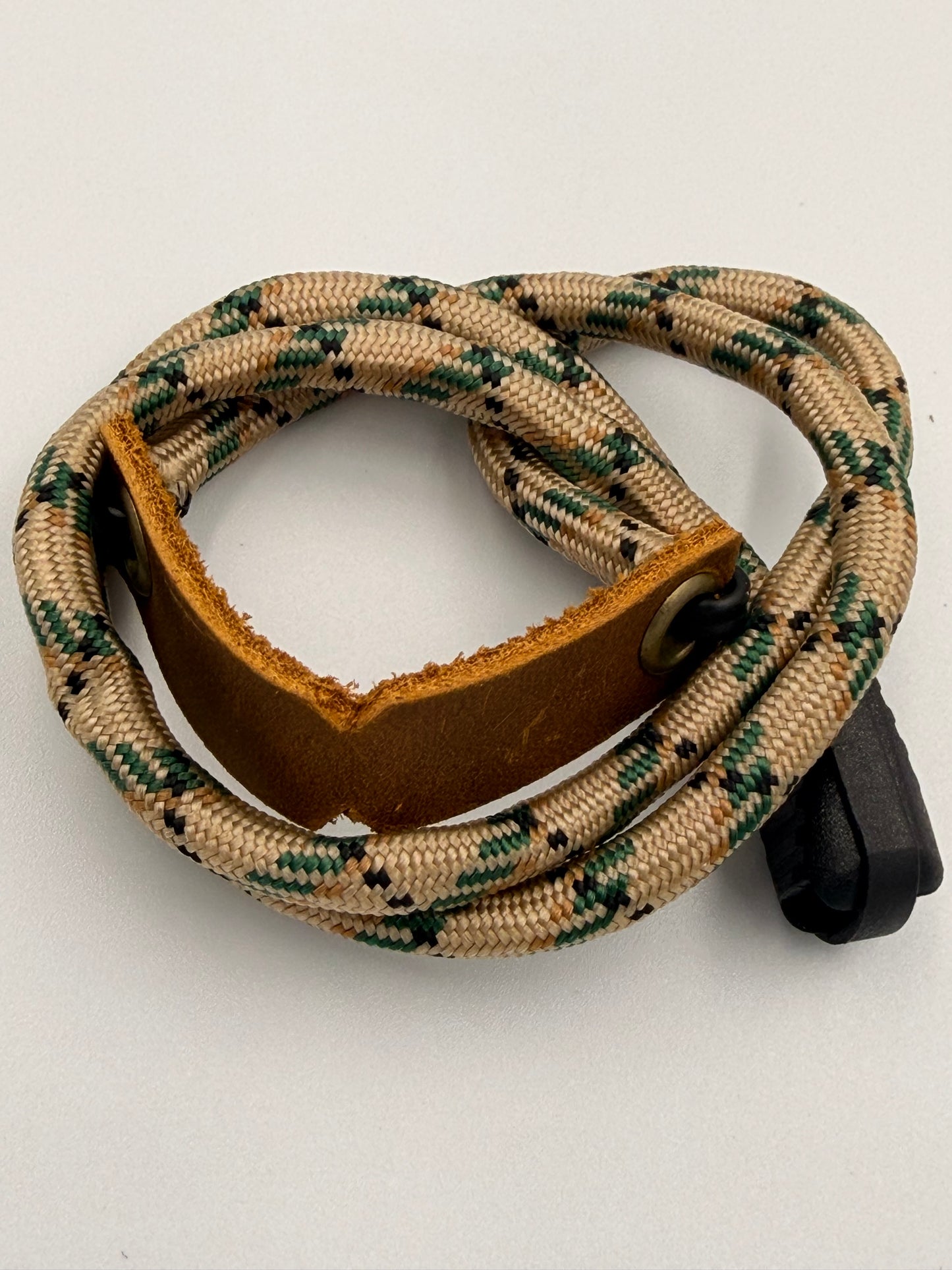 A coiled tan and green edc bracelet with a brown leather basket and a black plastic end cap, photographed on a plain light background.